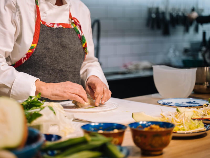 A person in chef's whites and an apron preparing food on a cutting board
